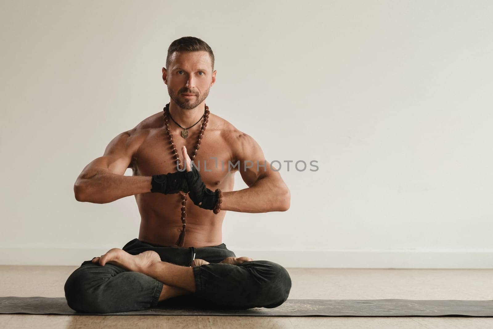 a man with a naked torso is sitting in the lotus position before doing yoga indoors. Fitness Trainer by Lobachad