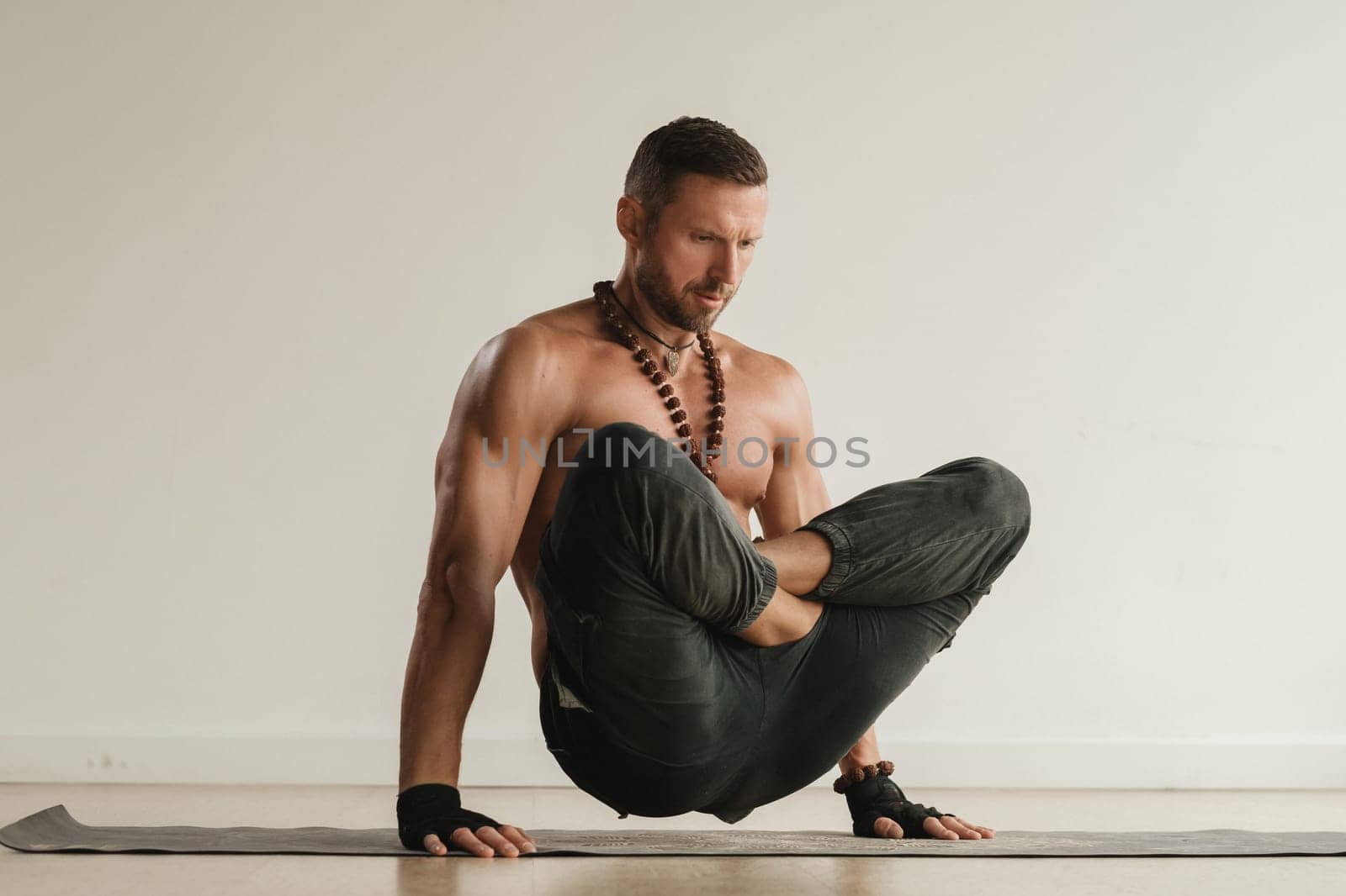 a man with a naked torso does yoga standing on his hands indoors. Fitness Trainer by Lobachad