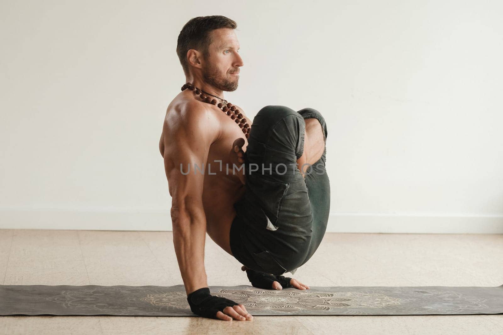 a man with a naked torso does yoga standing on his hands indoors. Fitness Trainer by Lobachad