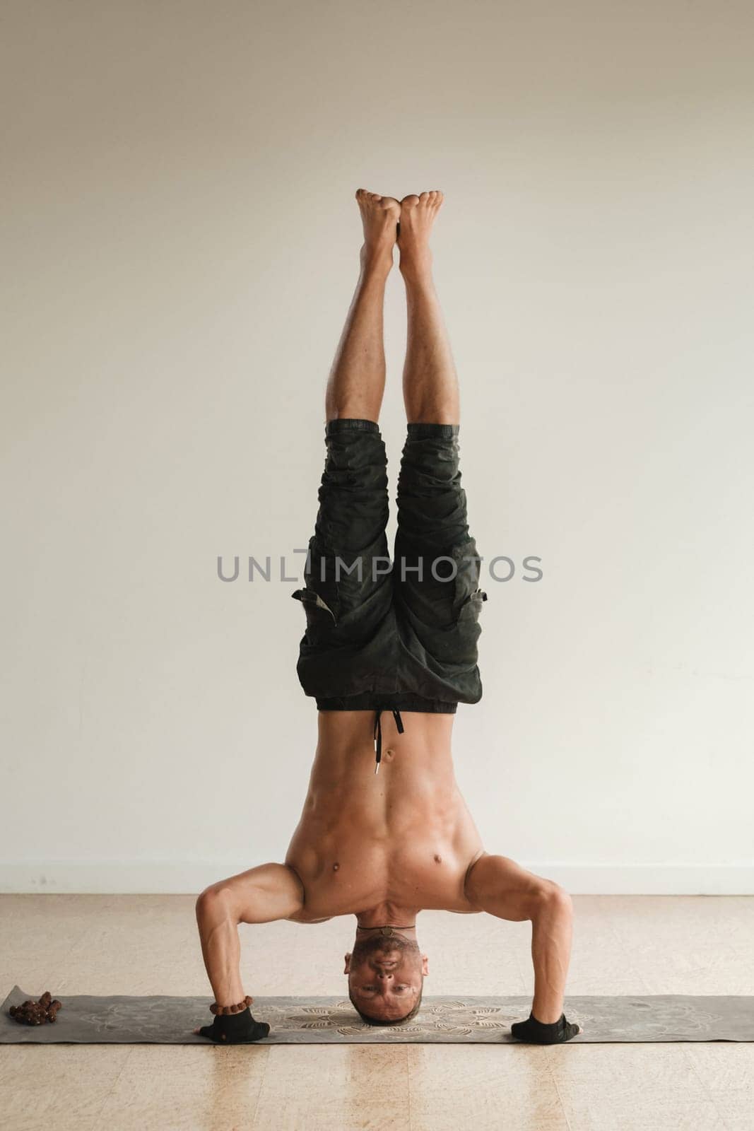 a man with a naked torso does yoga standing on his head indoors. Fitness Trainer by Lobachad