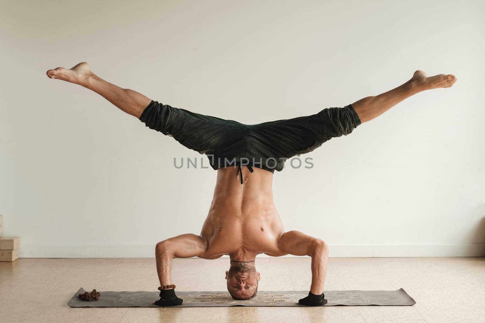 a man with a naked torso does yoga standing on his head indoors. Fitness Trainer.