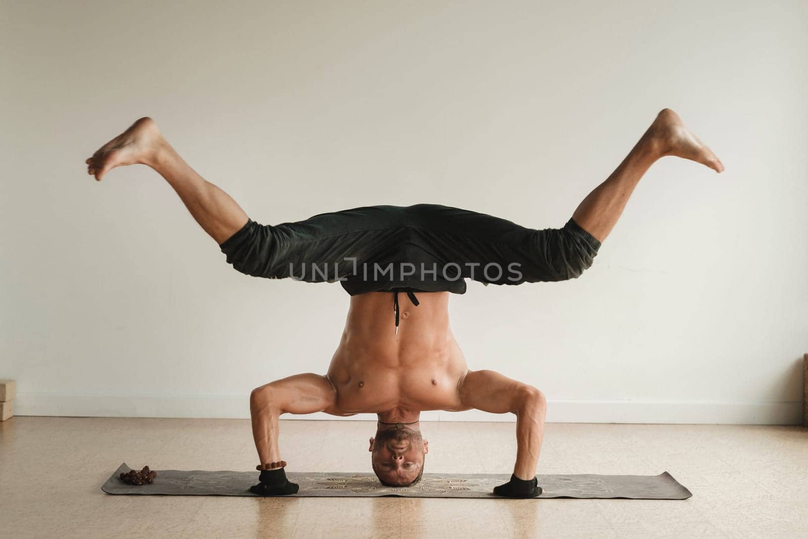 a man with a naked torso does yoga standing on his head indoors. Fitness Trainer by Lobachad