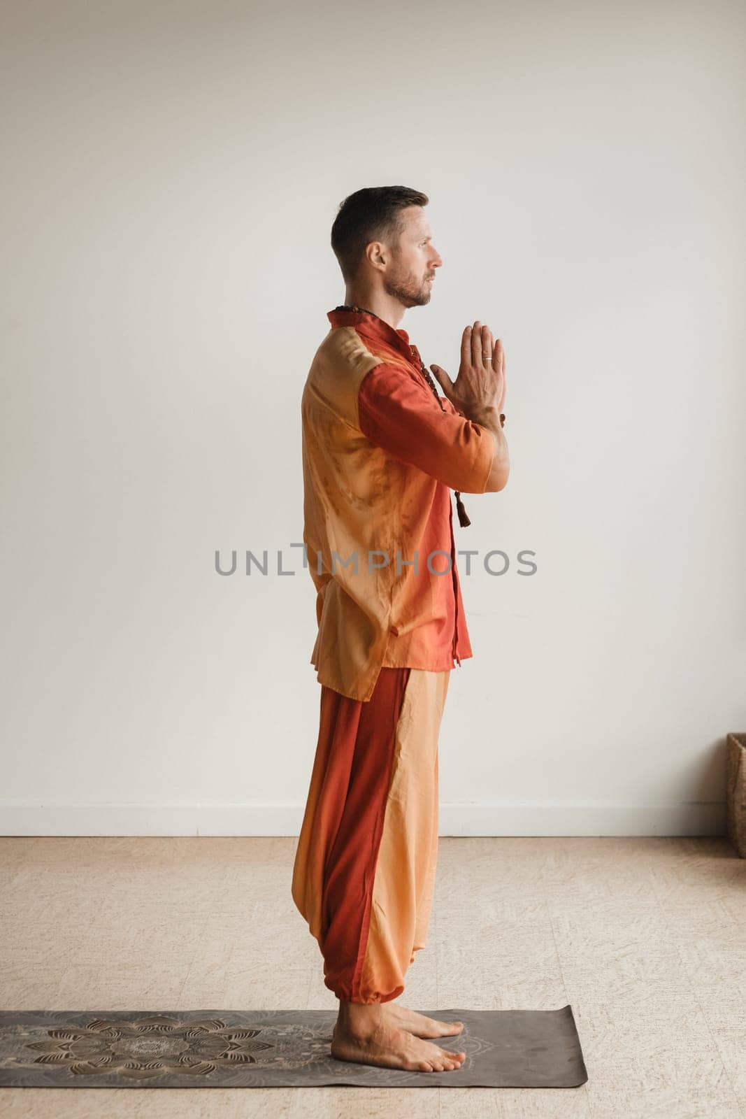 a man in an orange suit does yoga in a fitness room. The concept of health by Lobachad