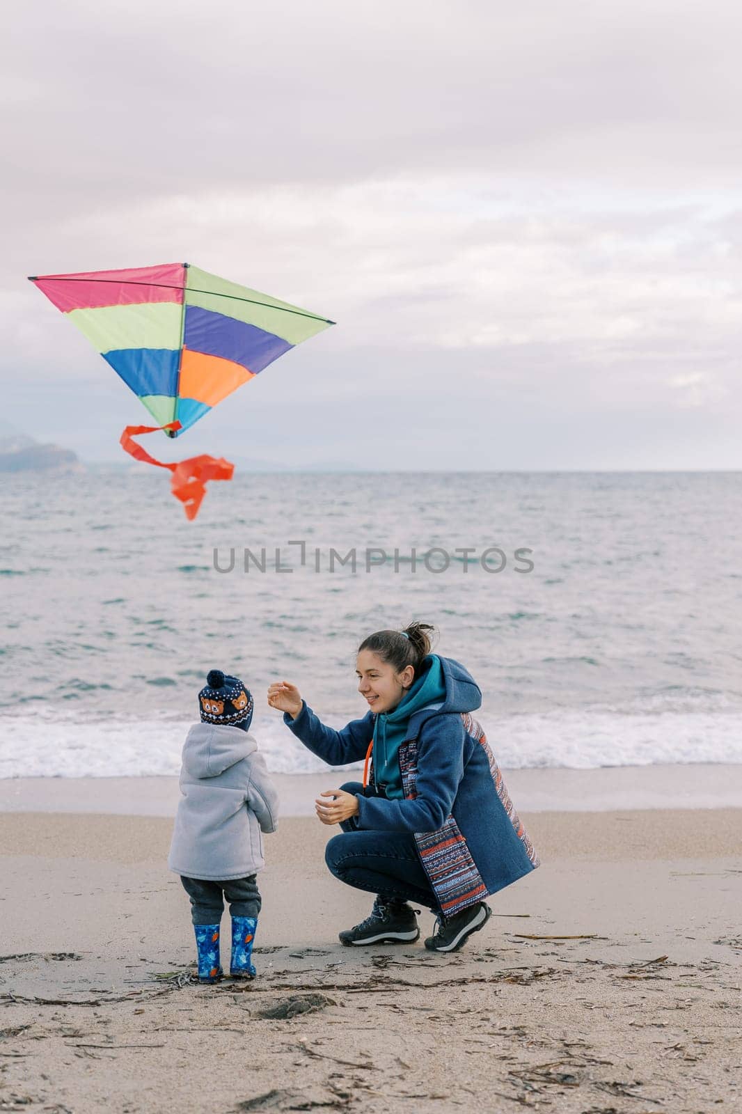 Mom crouched next to a little girl with a colorful kite in her hand near the sea. High quality photo