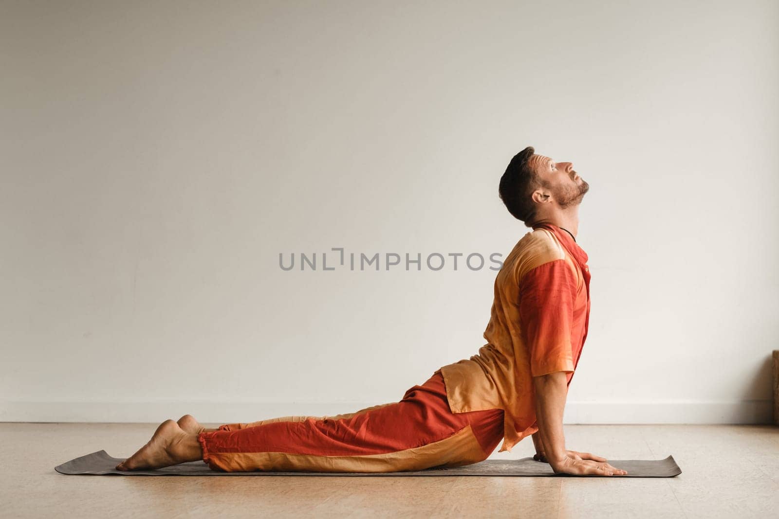 a man in an orange suit does yoga in a fitness room. The concept of health by Lobachad