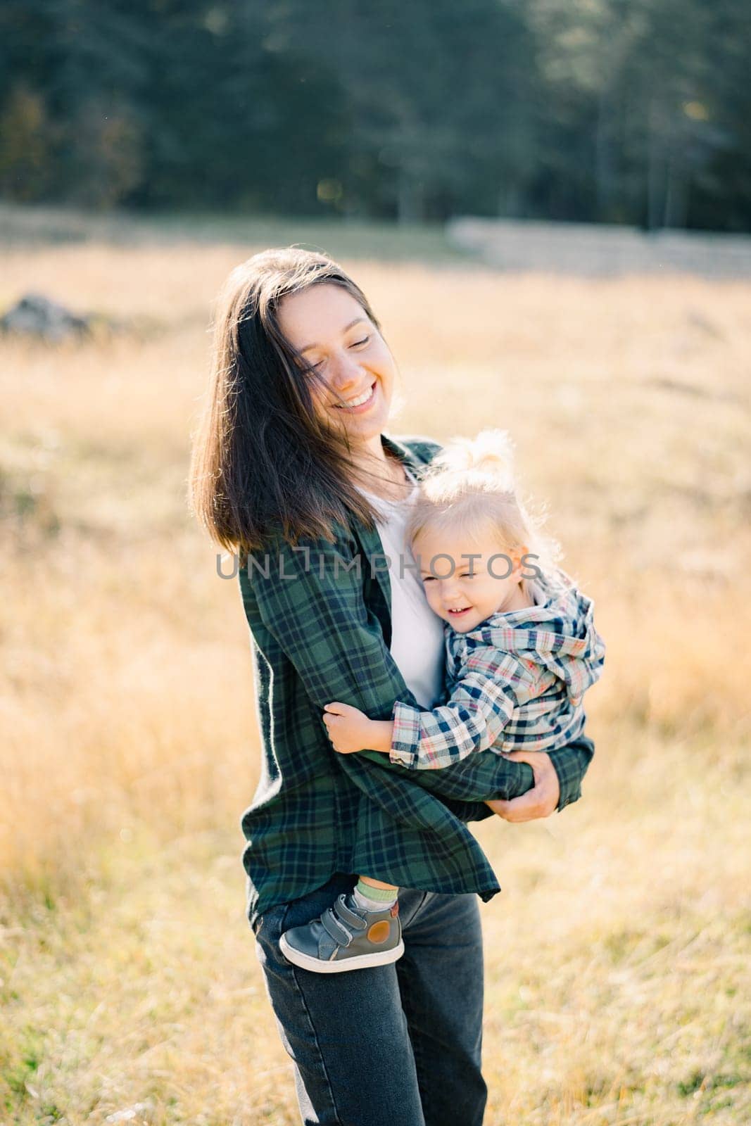 Smiling mom with a little girl in her arms stands on a sunny meadow by Nadtochiy