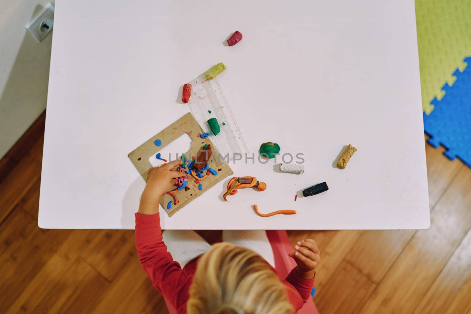 Little girl sculpts plasticine figures at the table. Top view. High quality photo