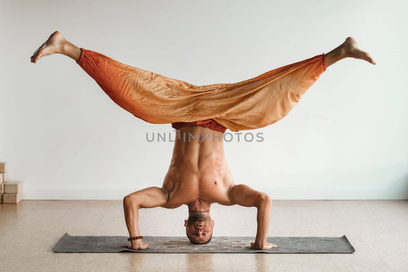 a man with a naked torso does yoga standing on his head indoors. Fitness Trainer by Lobachad