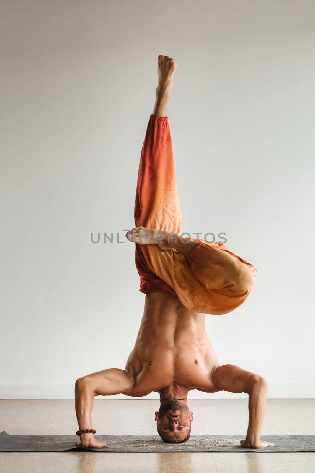 a man with a naked torso does yoga standing on his head indoors. Fitness Trainer.