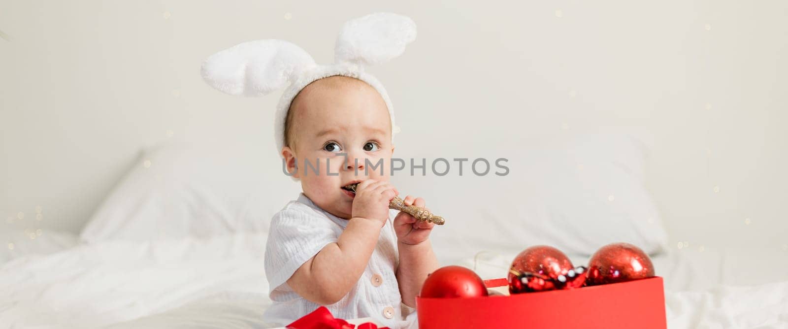Christmas Baby in Santa Hat Child playing with baubles. Present Gift Box over Holiday Lights background and Merry Christmas