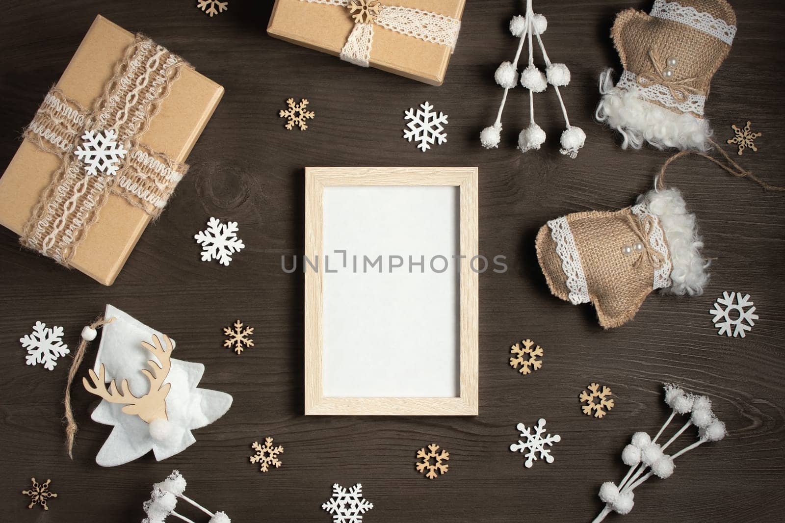 An empty frame on a wooden table surrounded by Christmas gifts and ornaments made of natural materials. A mockup for greeting cards and advertisements.