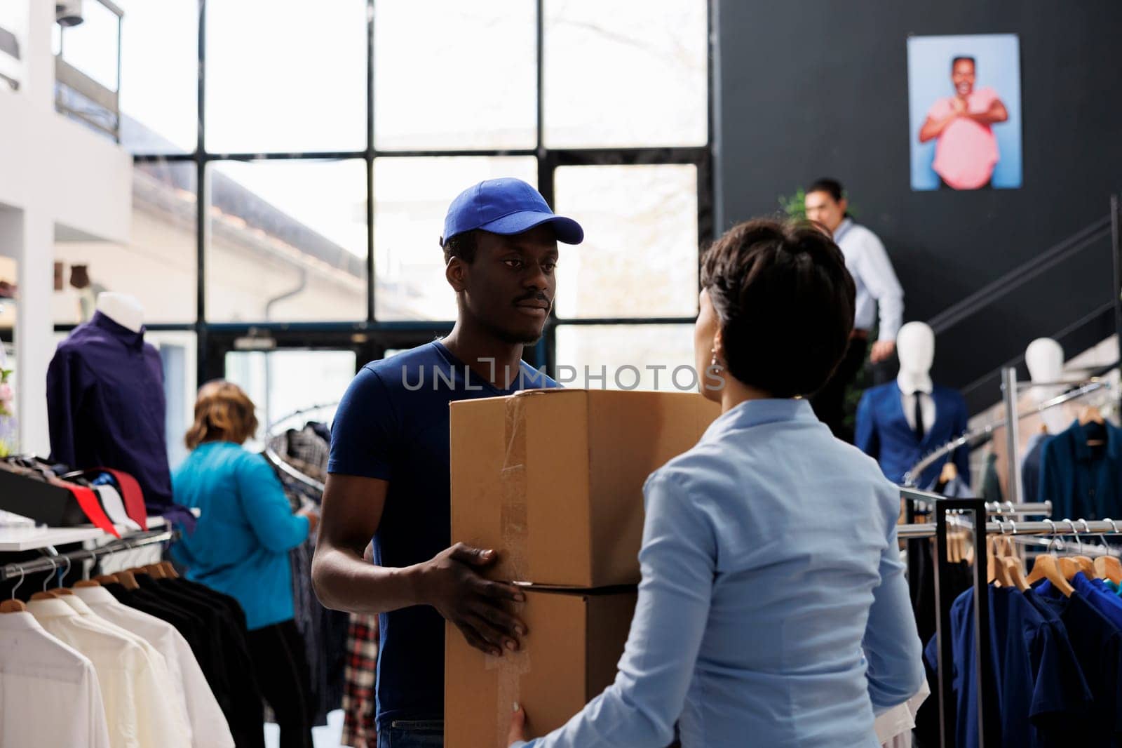 African american courier holding cardboard boxes, discussing shipping detalis with woman manager in shopping centre. Man in delivery uniform working with fashion store. Stylish boutique concept