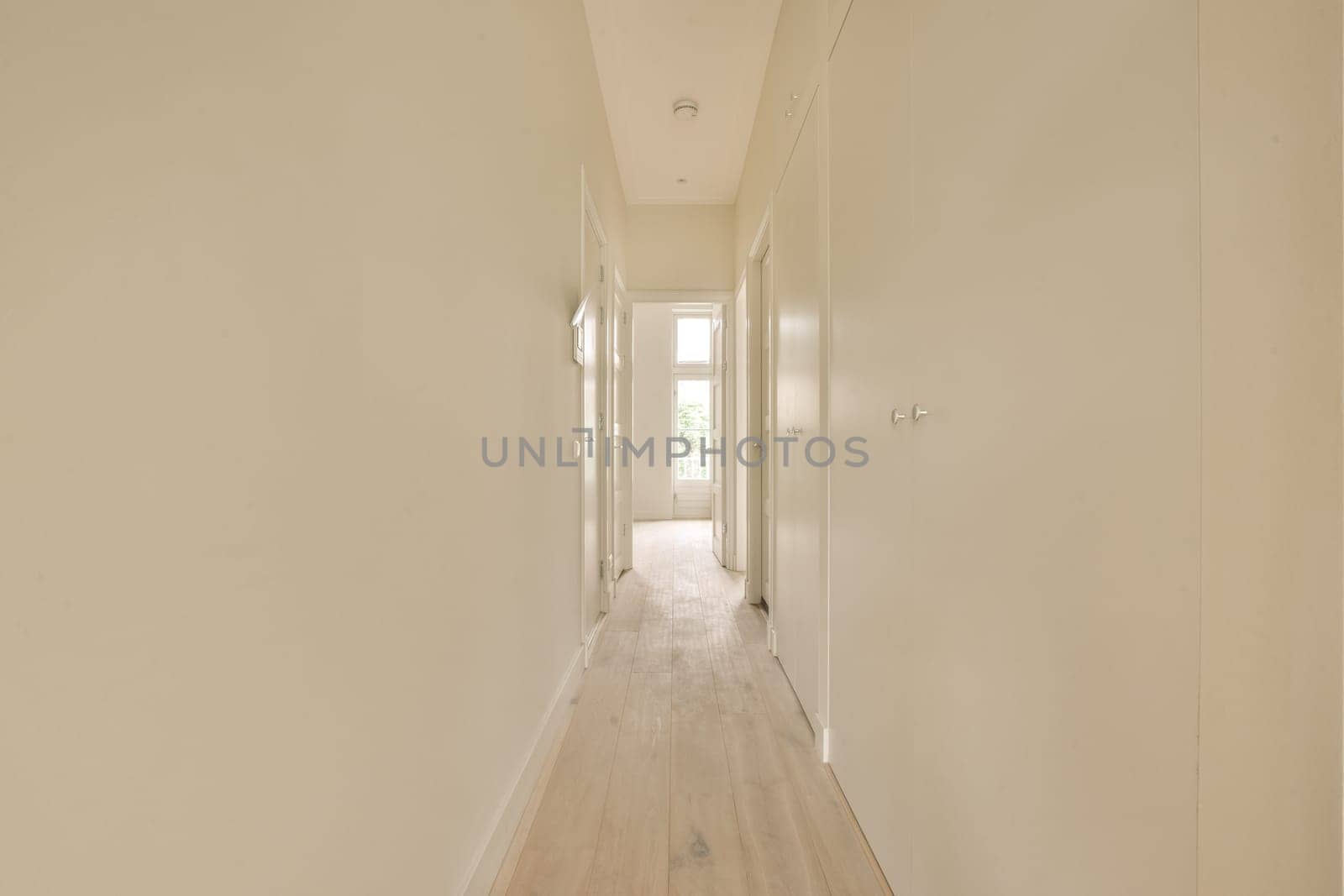 a long white hallway with white walls and wood floors by casamedia
