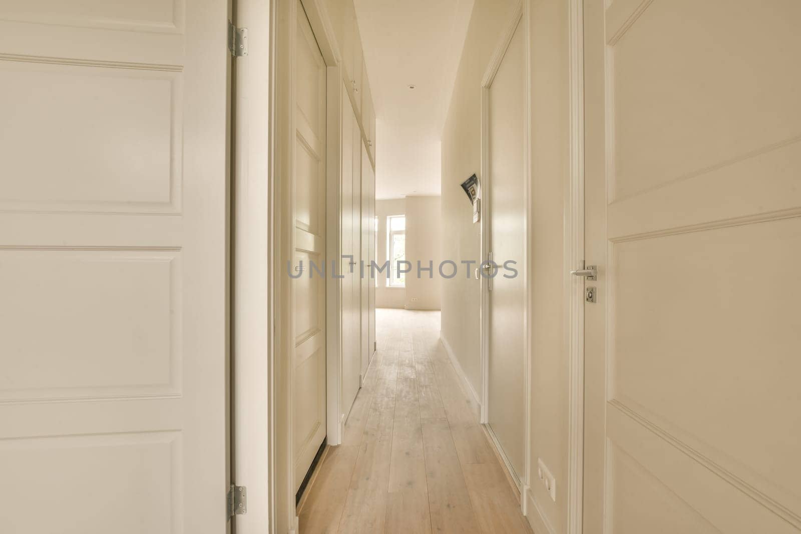 a long hallway with white walls and wood flooring on either side by side, leading to the other rooms