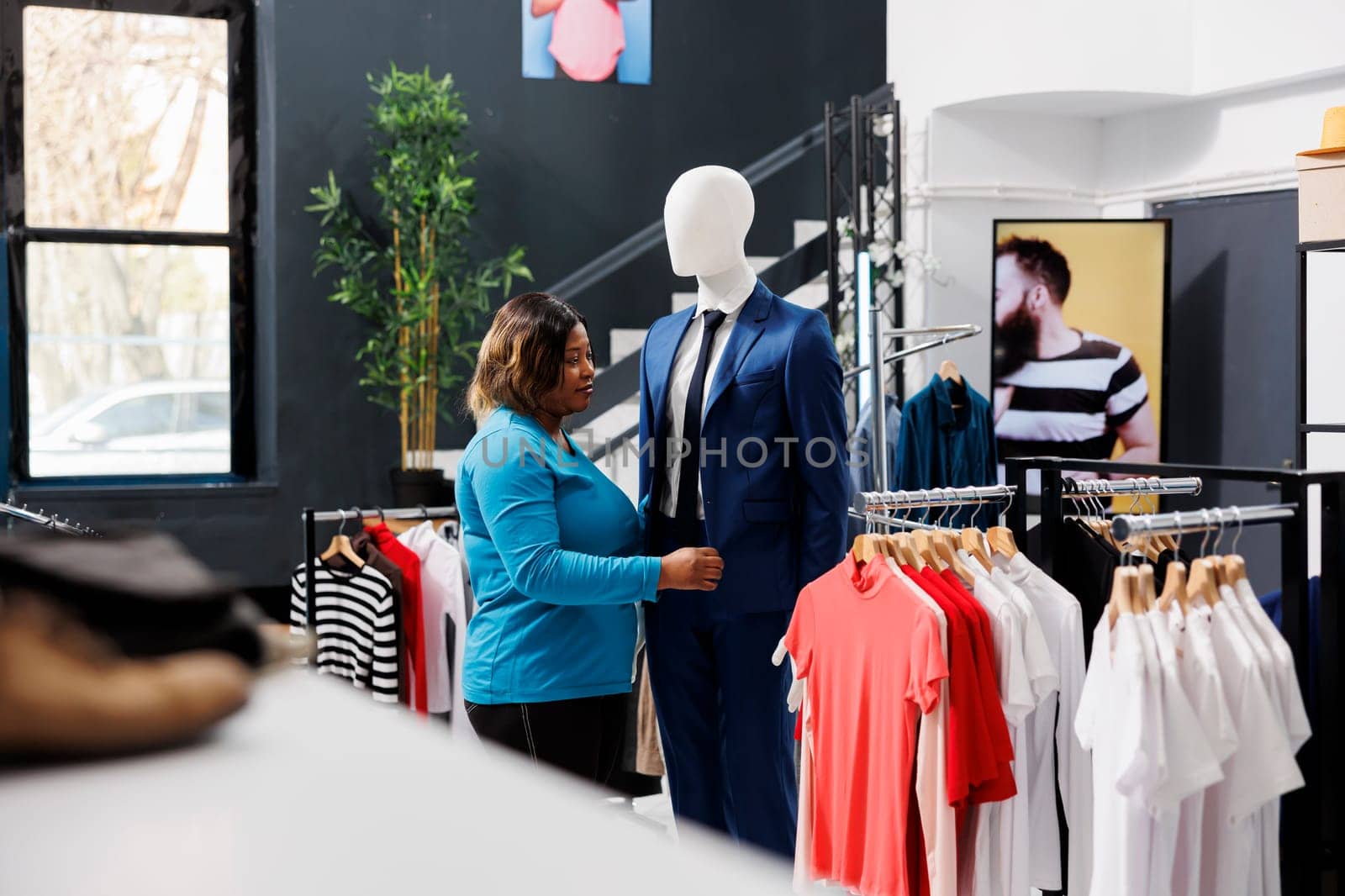 Stylish woman shopping for formal wear, looking at fashionable suit in clothing store. African american customer buying trendy merchandise, analyzing clothes fabric in modern boutique