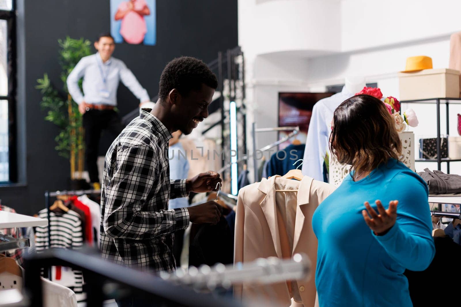 Stylish client shopping for fashion collection, looking at shirt fabric in modern boutique. African american couple buying fashionable clothes, checking hangers with formal wear in clothing store