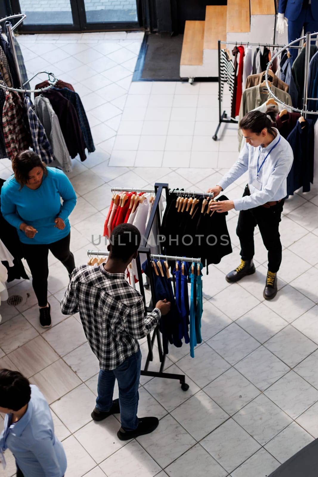 Top view of stylish people shopping for casual wear in modern boutique, buying clothes from new fashion collection. Diverse shoppers looking at hangers full with fashionable merchandise in store
