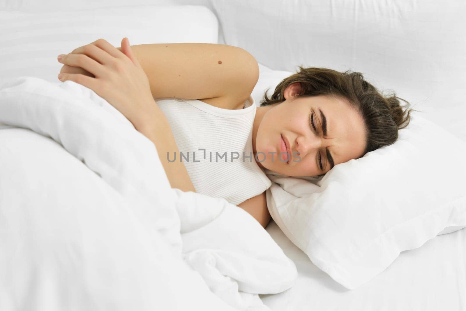 Young woman lying in bed with stomach ache, has painful cramps, menstrual pain. Lifestyle and wellbeing concept