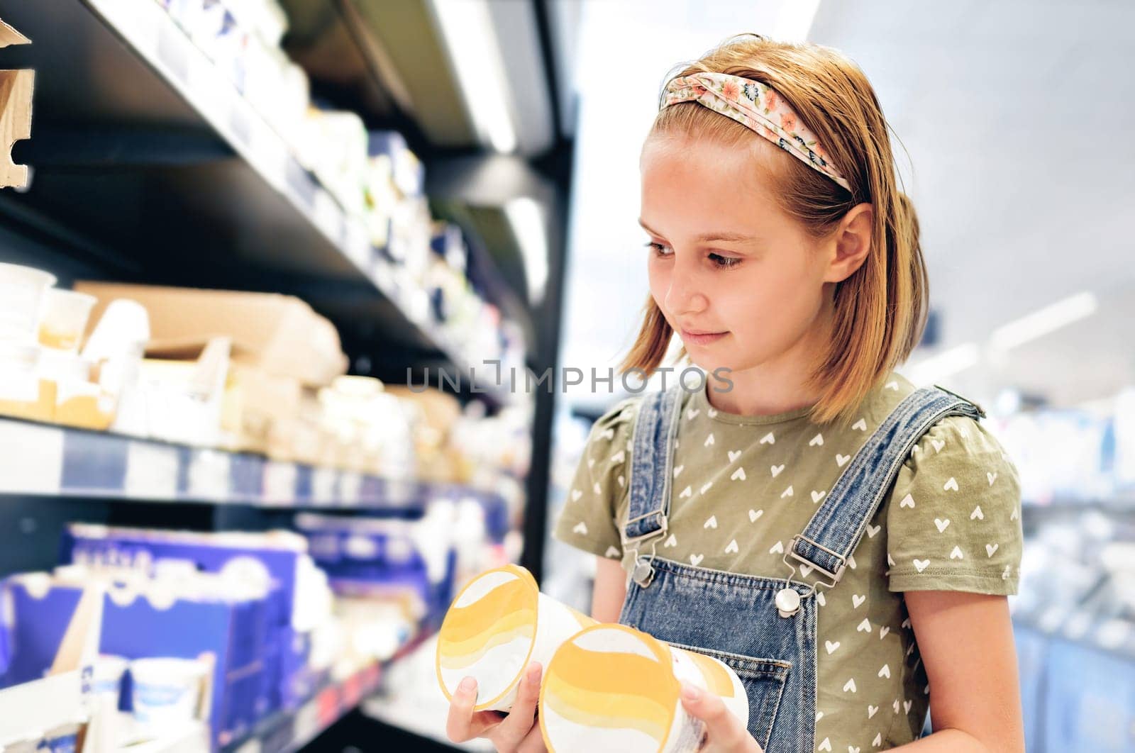 Pretty girl child choosing yogurt in supermarket shop. Beautiful female preteen kid looking milk products in grocery store