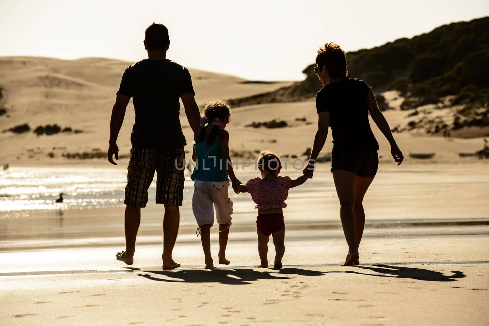 Happy family with children silhouette at sea beach sunset. Father, mother and kids walking on seashore at sunset