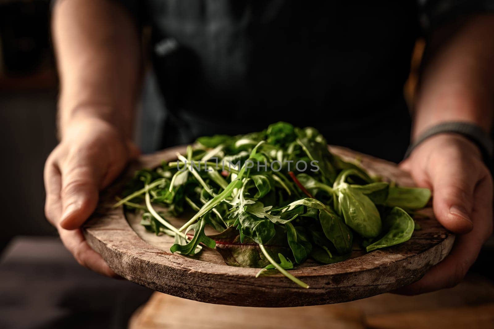 Chief hands serve fresh green salad leaves with arugula, lettuce, spinach and beets mix on wooden rustic plate. Vegetarian organic plant food