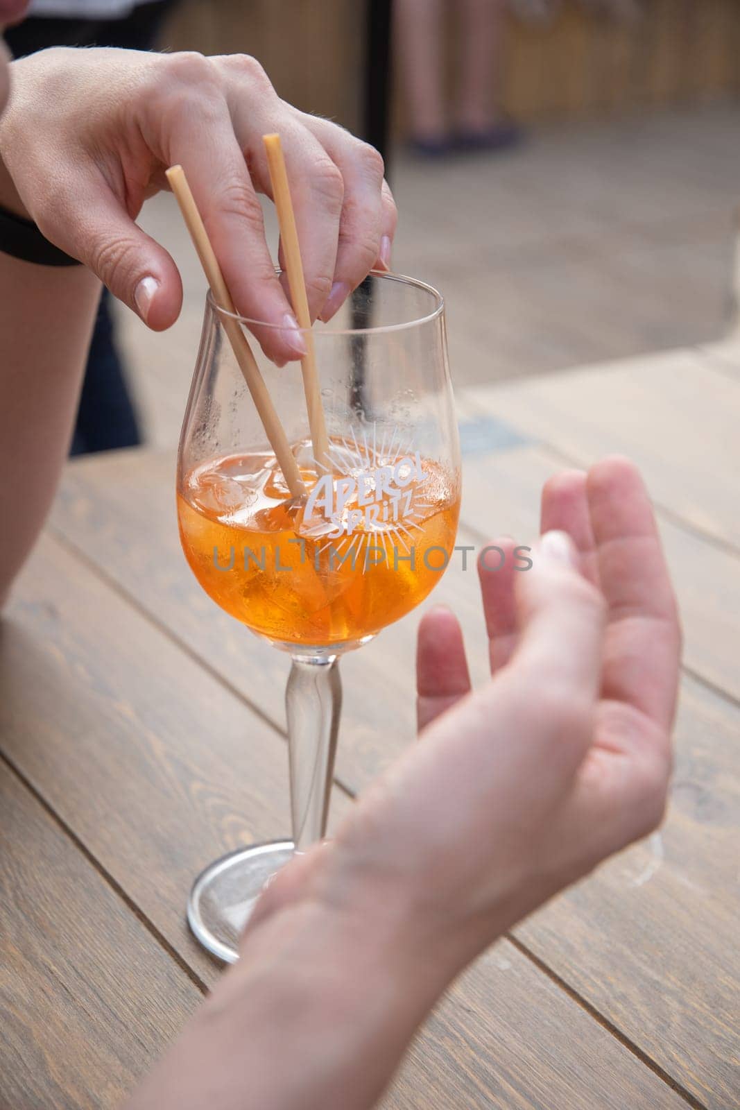 a young woman sitting at a table in a summer cafe with a glass of iced drink,cold exotic cocktail,in sunny golden time, tourist drinking cool lemonade, High quality photo