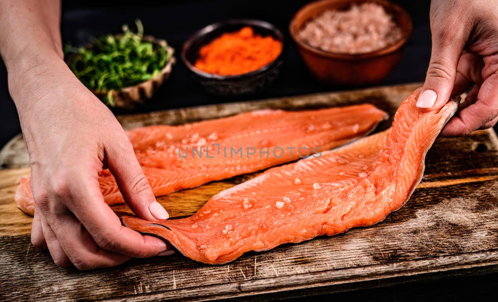 Woman cooking fillet trout with herbs and salt for dinner. Fresh red fish healthy food.