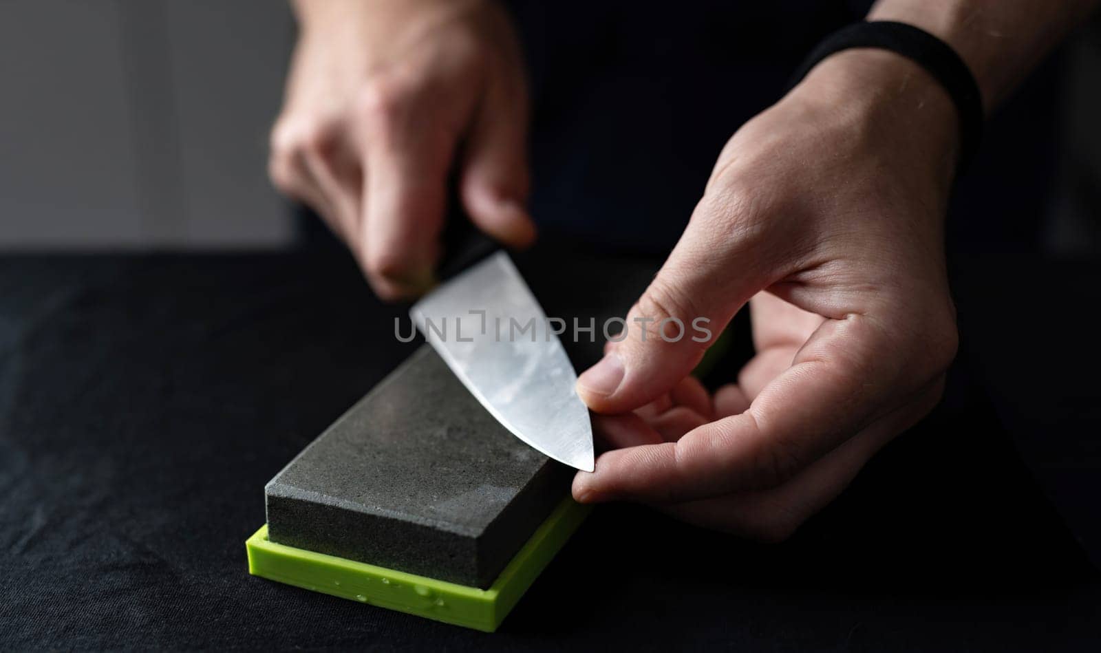 Man Uses Natural Sharpening Whetstone To Sharpen Big Kitchen Knife Against Black Background