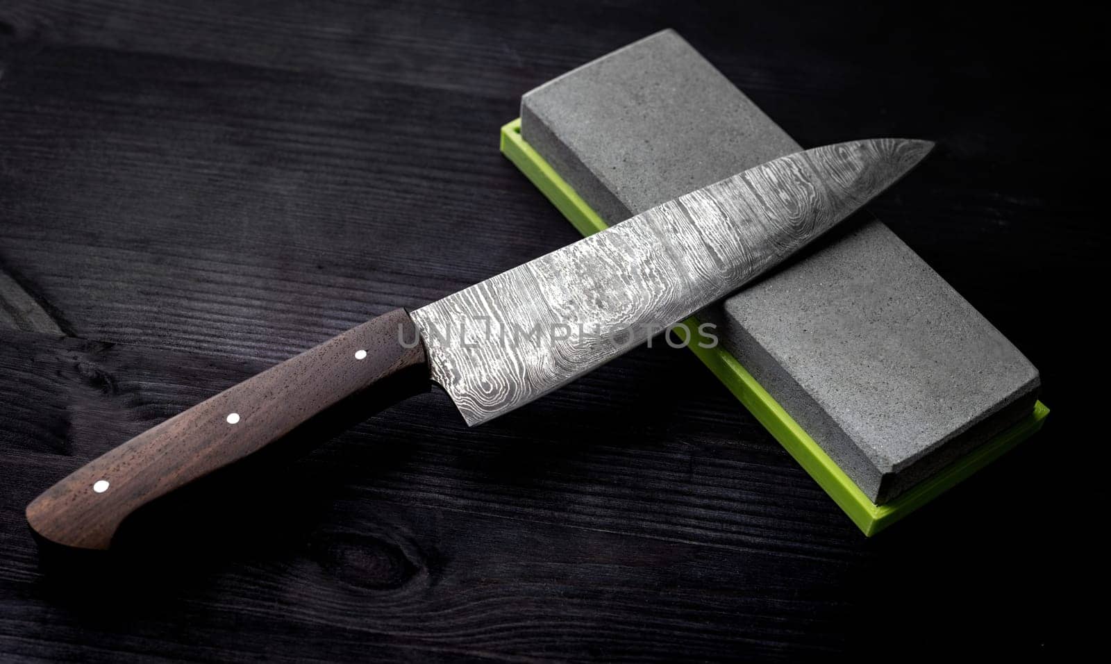 Big Kitchen Knife Rests On Sharpening Stone On Kitchen Table Against Black Background