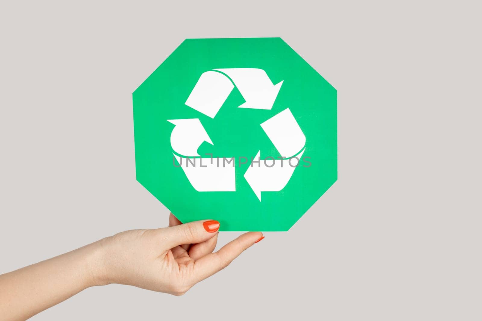Closeup of woman hand showing green recycling sign, environment protection. Indoor studio shot isolated on gray background.