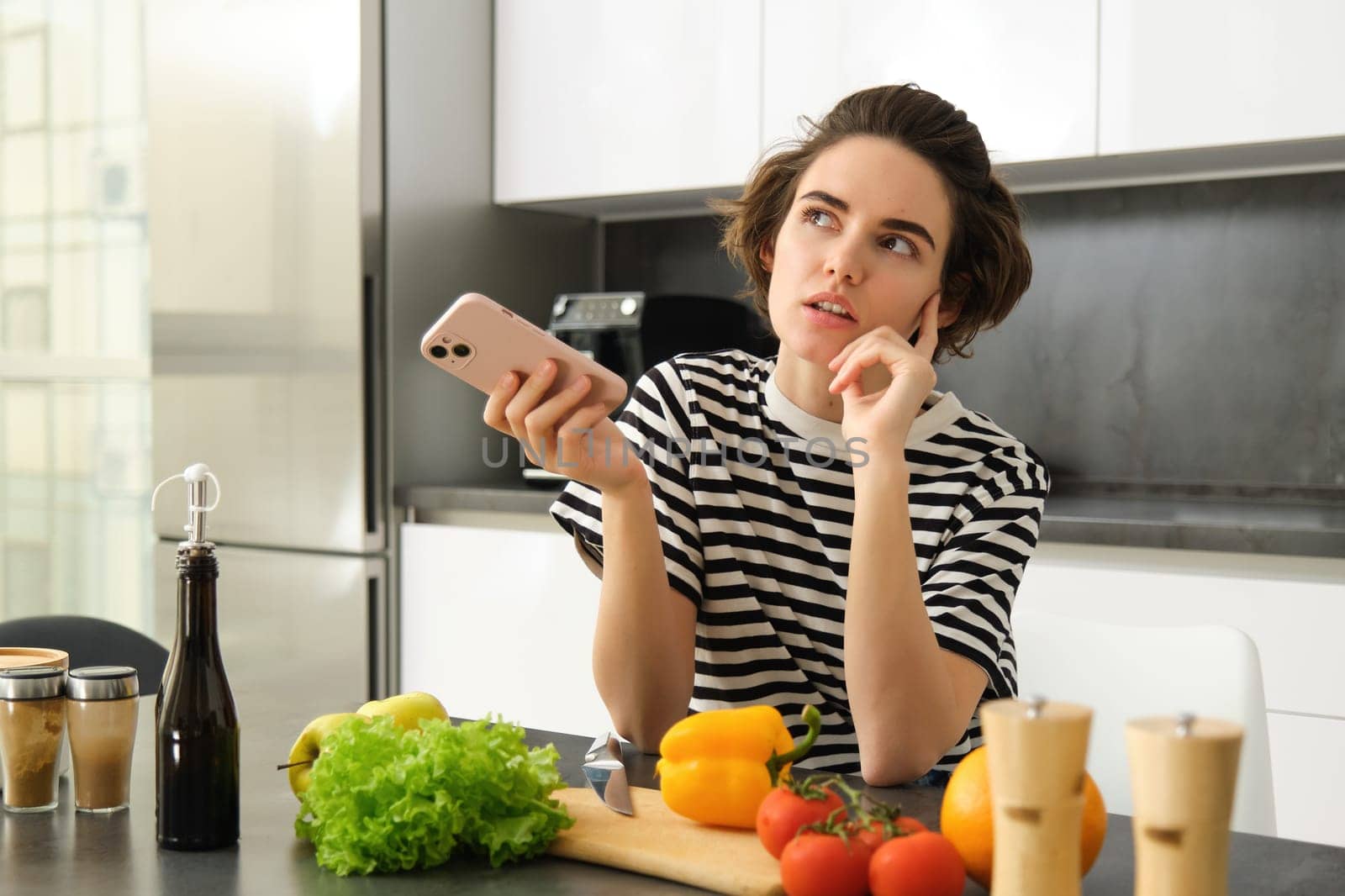 Portrait of young woman food blogger, posting on social media recipe, vegan salad, standing in the kitchen with smartphone, chopping vegetables by Benzoix