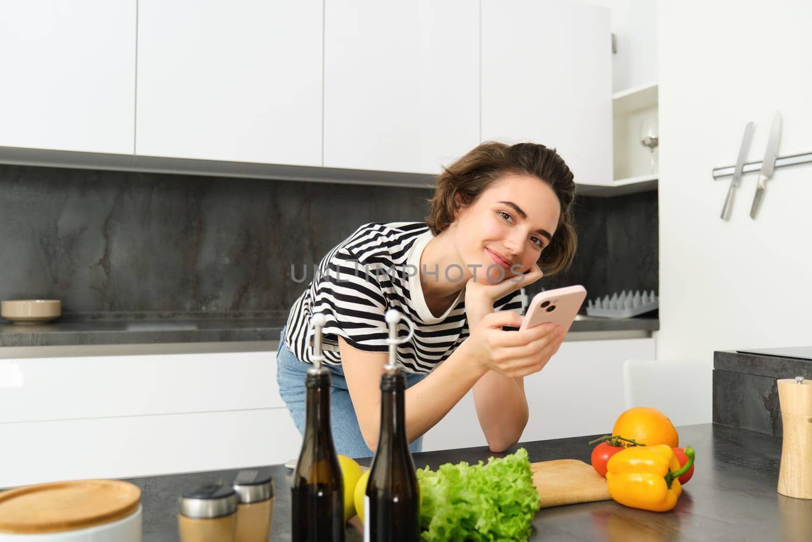 Portrait of woman, lifestyle blogger, posting picture of her cooking process on smartphone app, standing near vegetables and chopping board by Benzoix