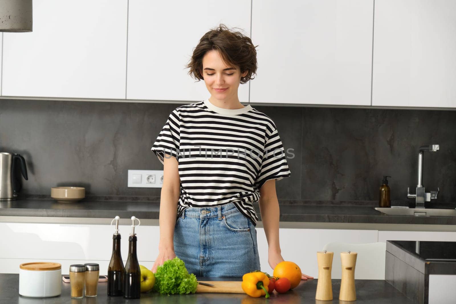 Portrait of young woman cooking salad. Cute girl vegan chopping vegetables on kitchen counter, preparing food by Benzoix