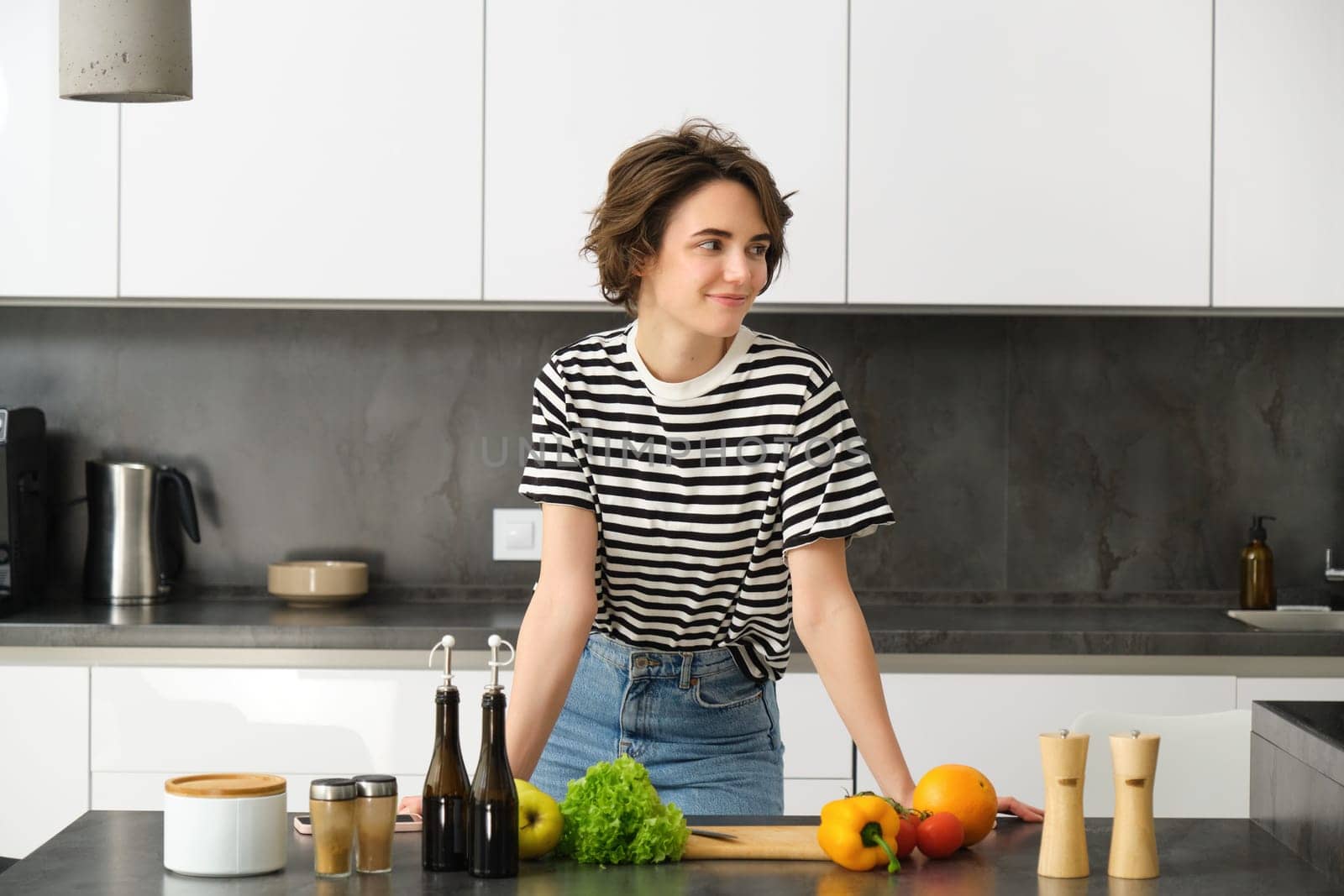 Portrait of smiling cute young woman making breakfast, chopping vegetables in the kitchen, preparing vegan meal by Benzoix