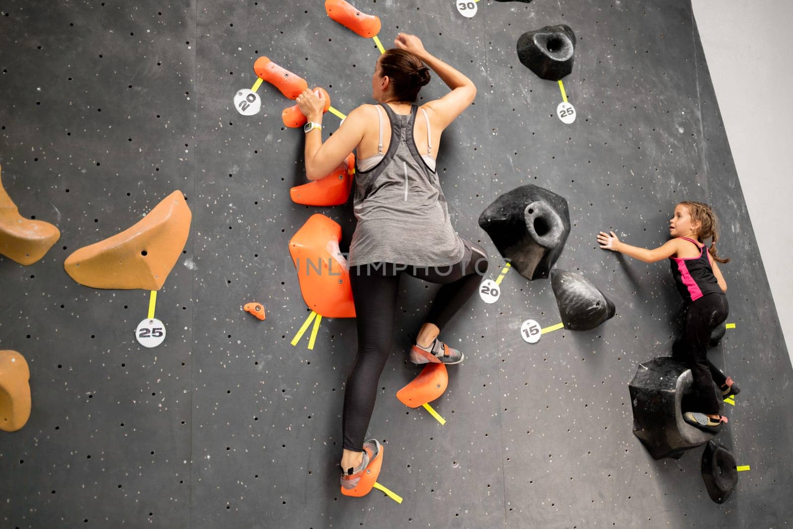 Mother and daughter climbing wall in gym by andreonegin