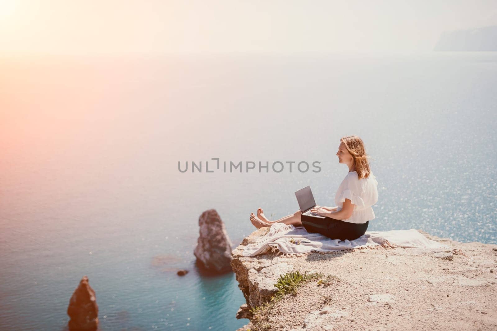 Successful business woman in yellow hat working on laptop by the sea. Pretty lady typing on computer at summer day outdoors. Freelance, travel and holidays concept.