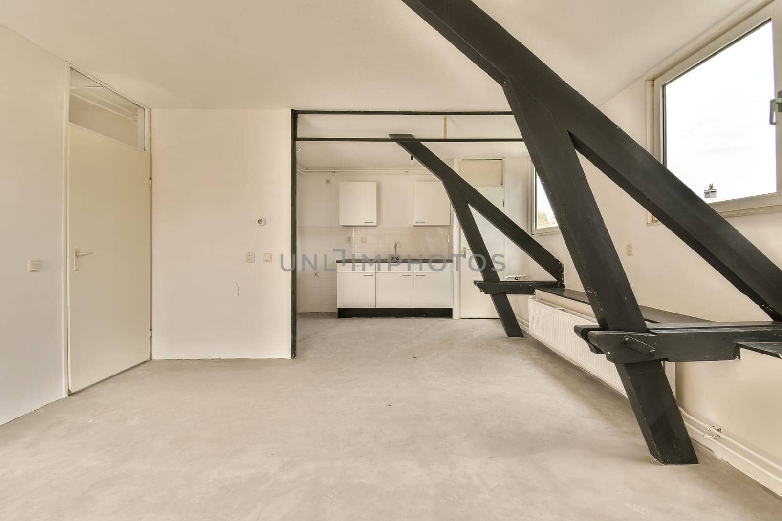 an empty room with white walls and black metal railings on the wall, there is a kitchen in the background