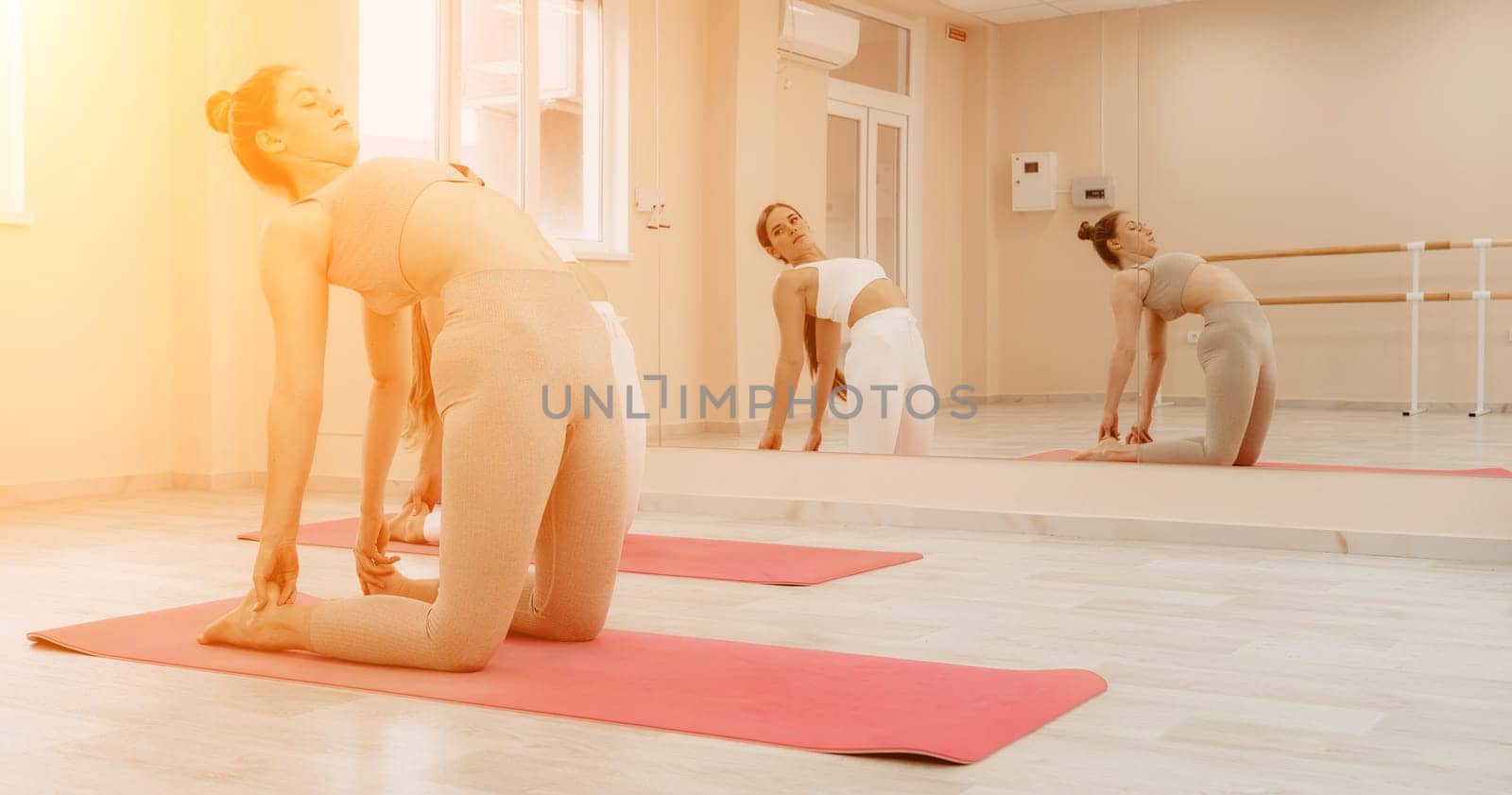 Group of young womans fitness instructor in Sportswear Leggings and Tops, stretching in the gym before pilates, on a yoga mat near the large window on a sunny day, female fitness yoga routine concept.