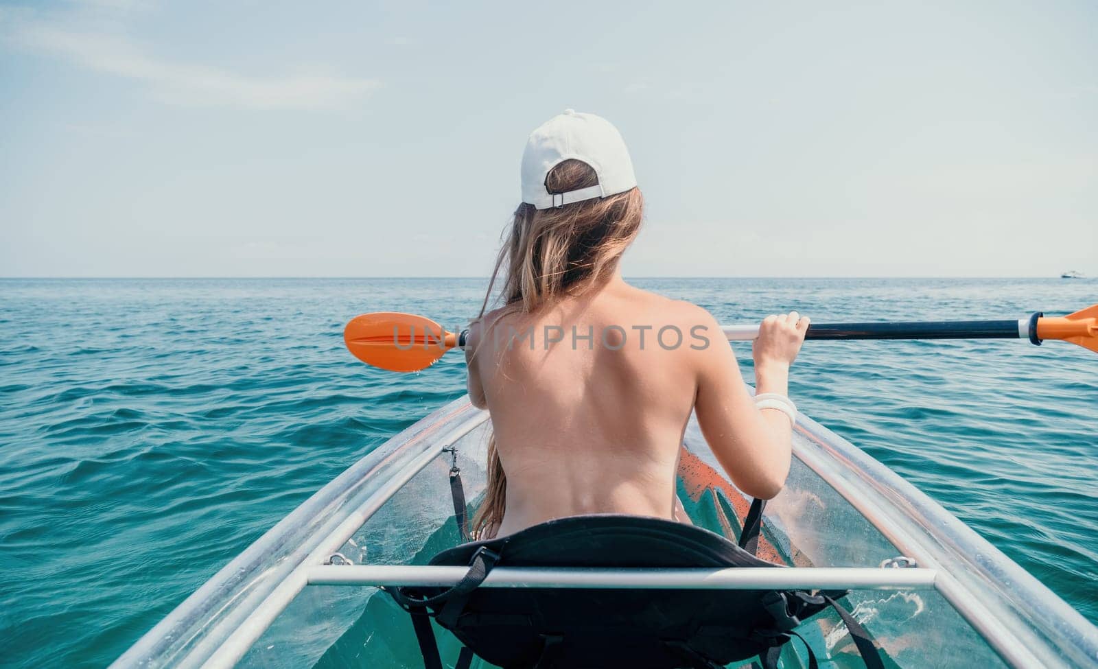 Woman in kayak back view. Happy young woman with long hair floating in transparent kayak on the crystal clear sea. Summer holiday vacation and cheerful female people having fun on the boat.