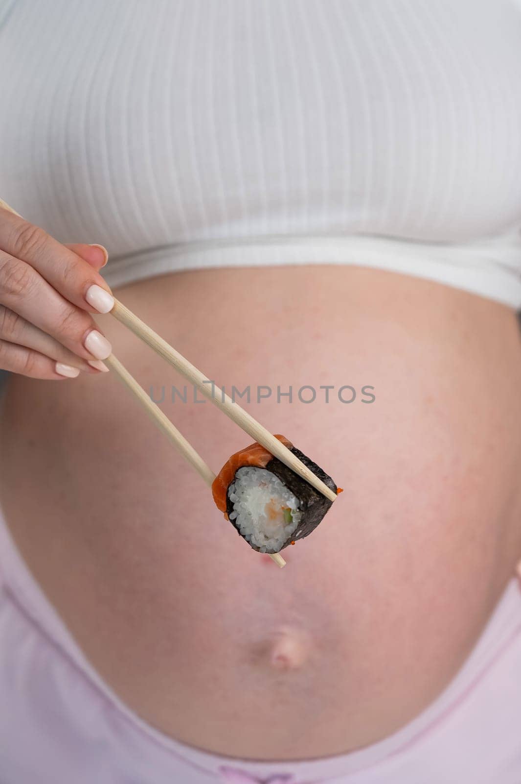 A pregnant woman holds a roll with chopsticks. Close-up of the belly. by mrwed54