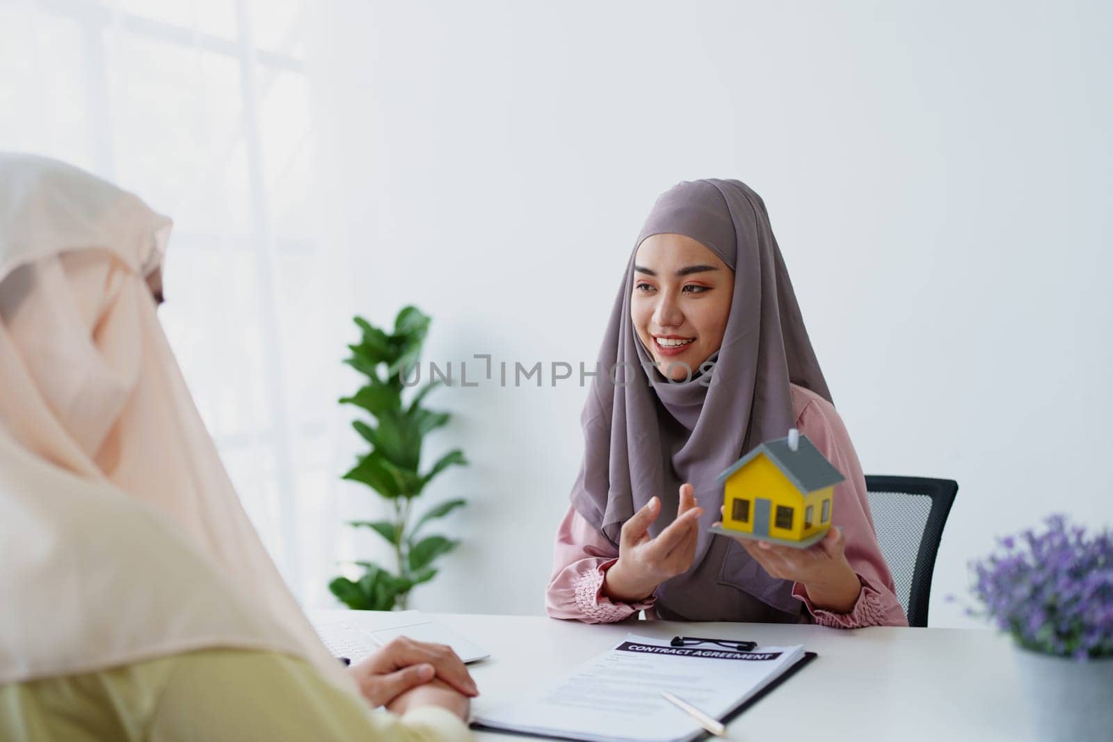 A female Muslim bank employee, making an agreement on a residential loan with a customer. by Manastrong