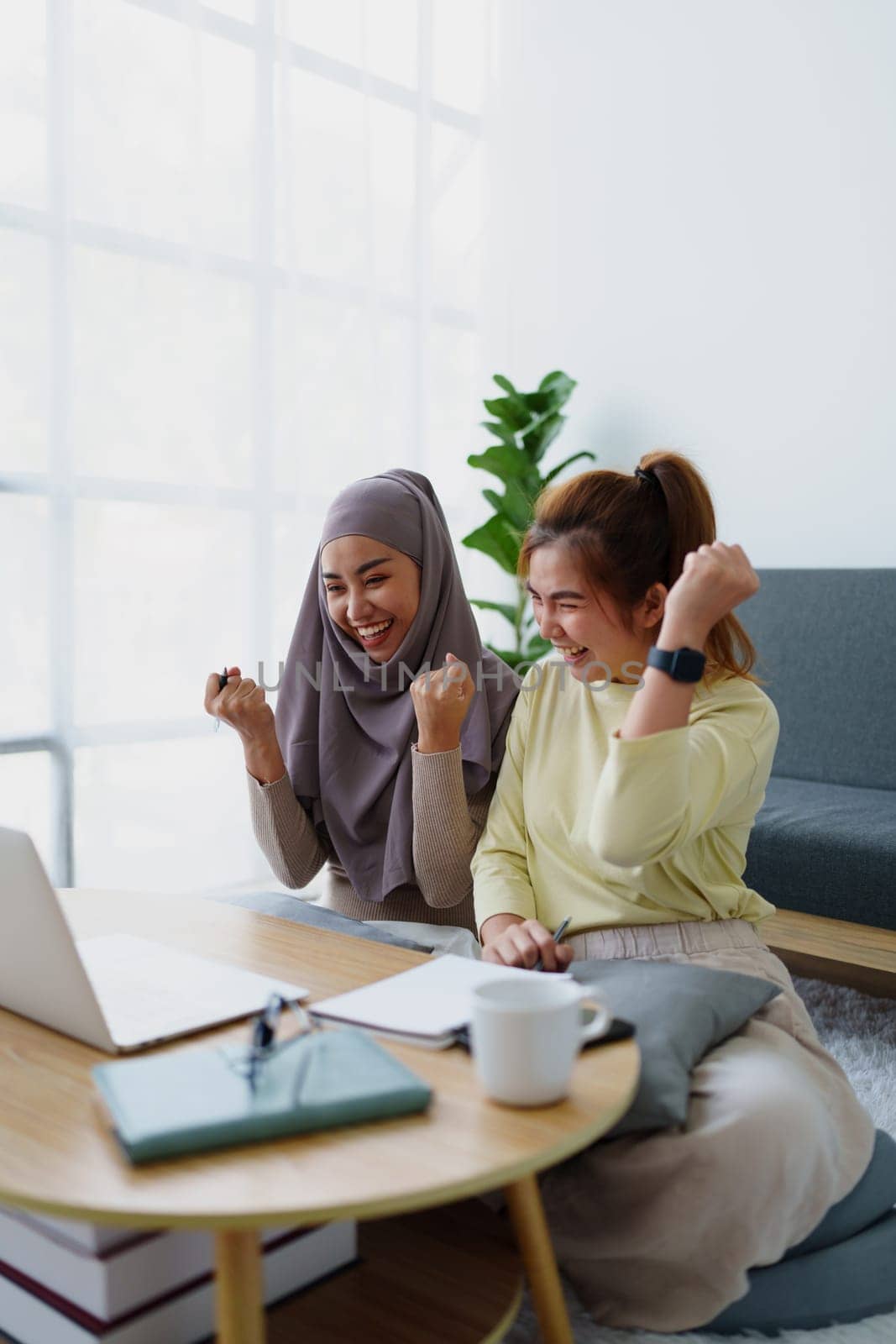 Muslim undergraduate students and Asian women express their joy after completing online study using a computer. by Manastrong