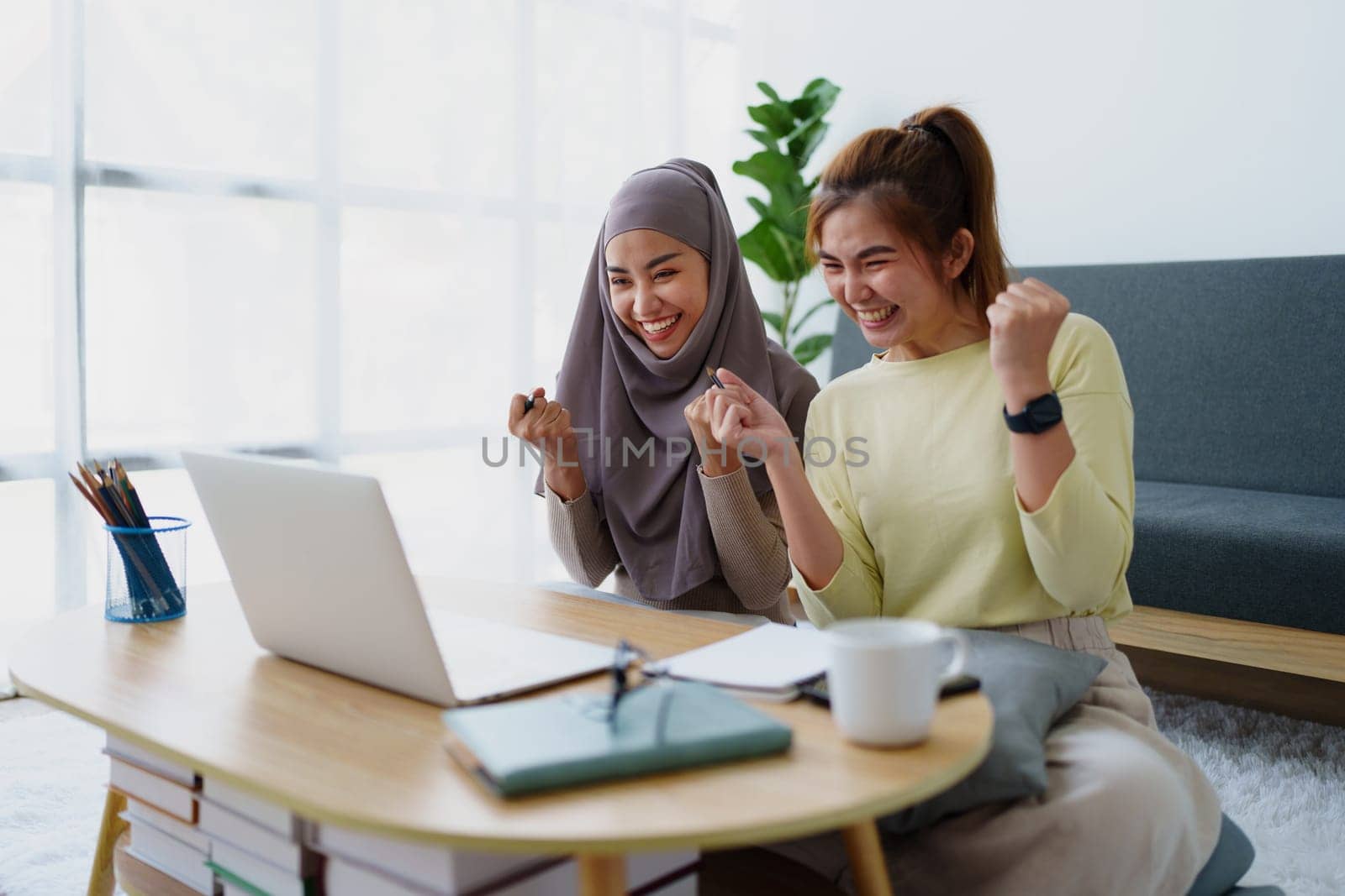 Muslim undergraduate students and Asian women express their joy after completing online study using a computer. by Manastrong