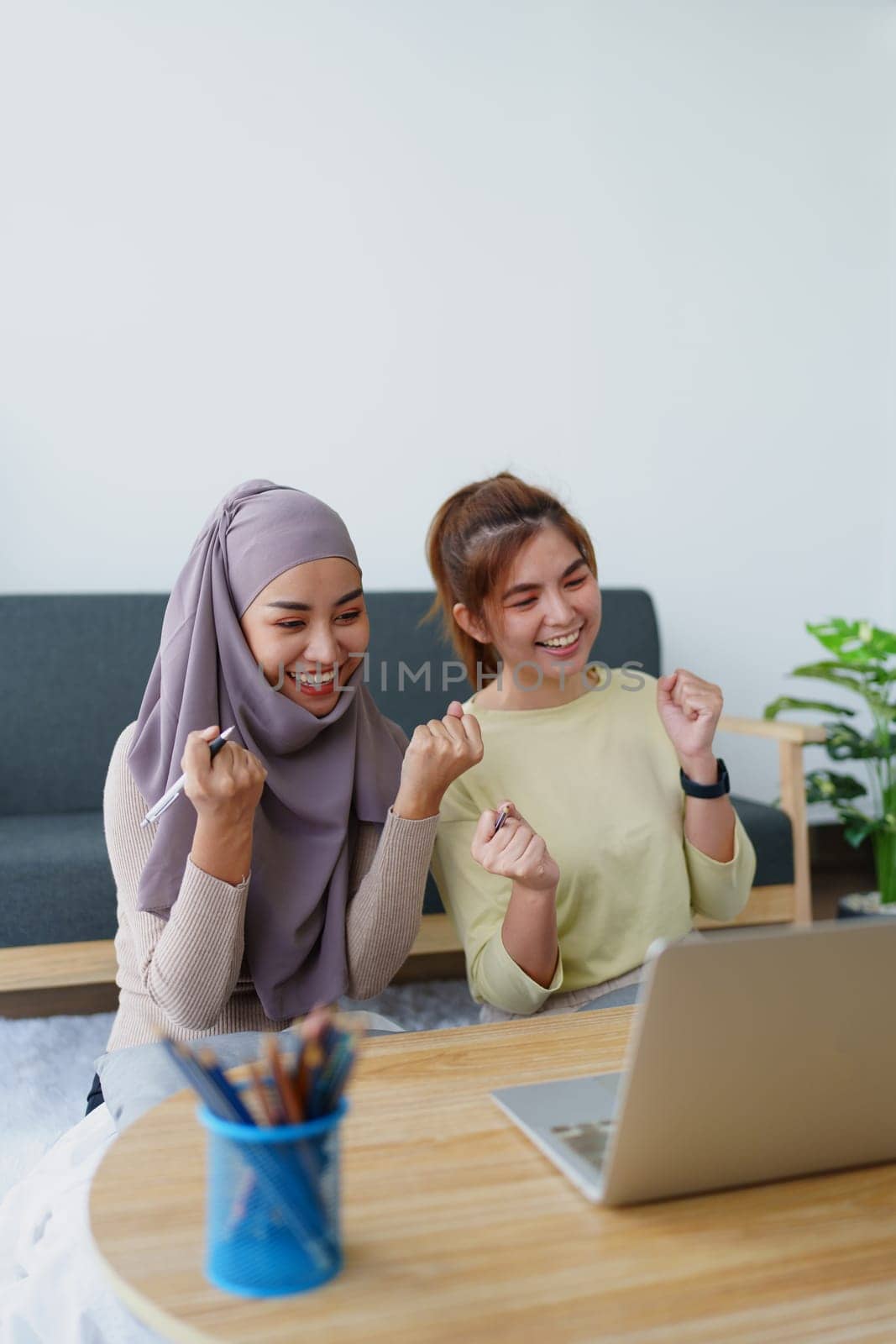 Muslim undergraduate students and Asian women express their joy after completing online study using a computer