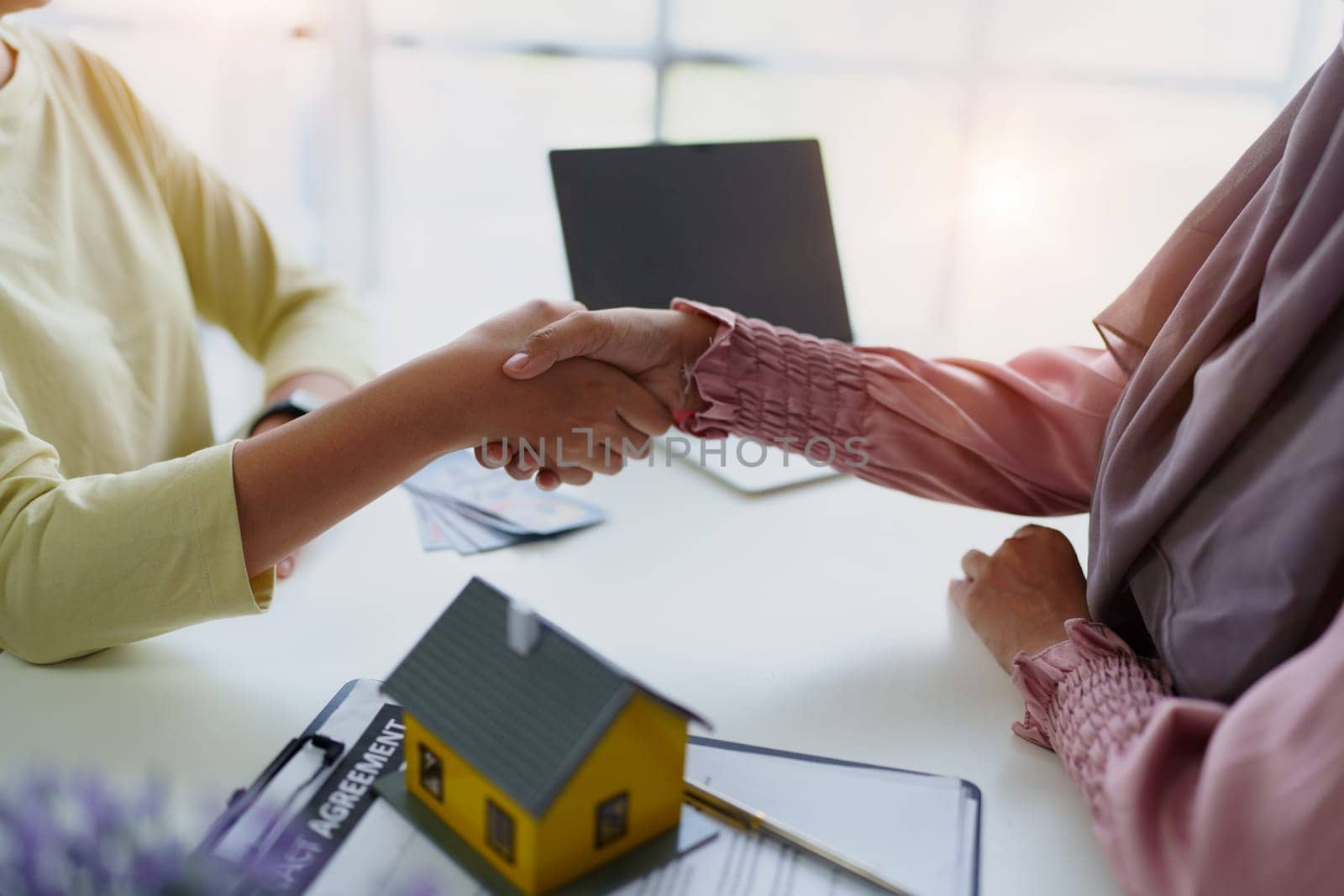 A female Muslim bank employee, holding hands, negotiates a residential loan with a customer