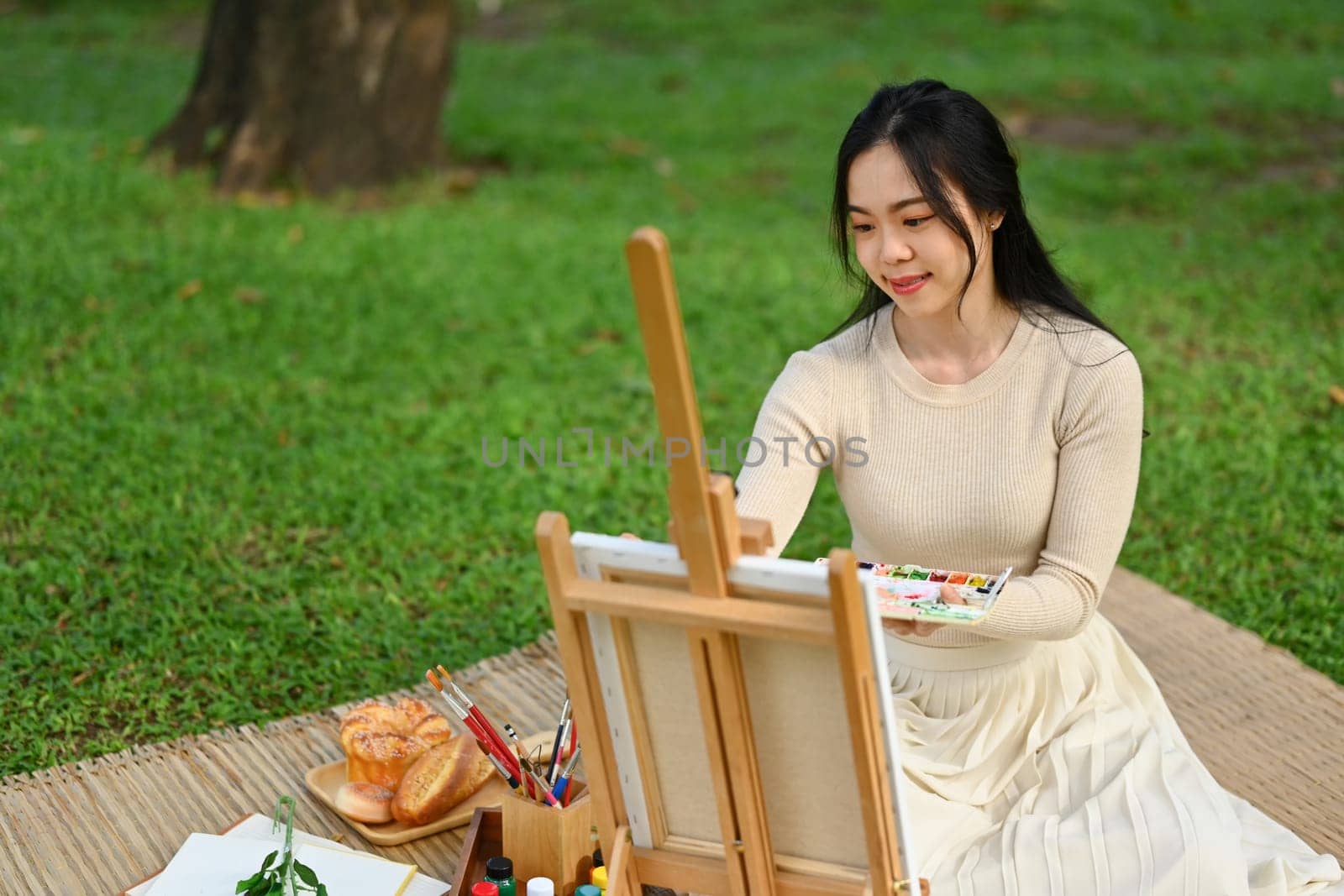 Attractive young woman painting picture on easel outdoors. Mindfulness, art therapy and creative hobbies concept.