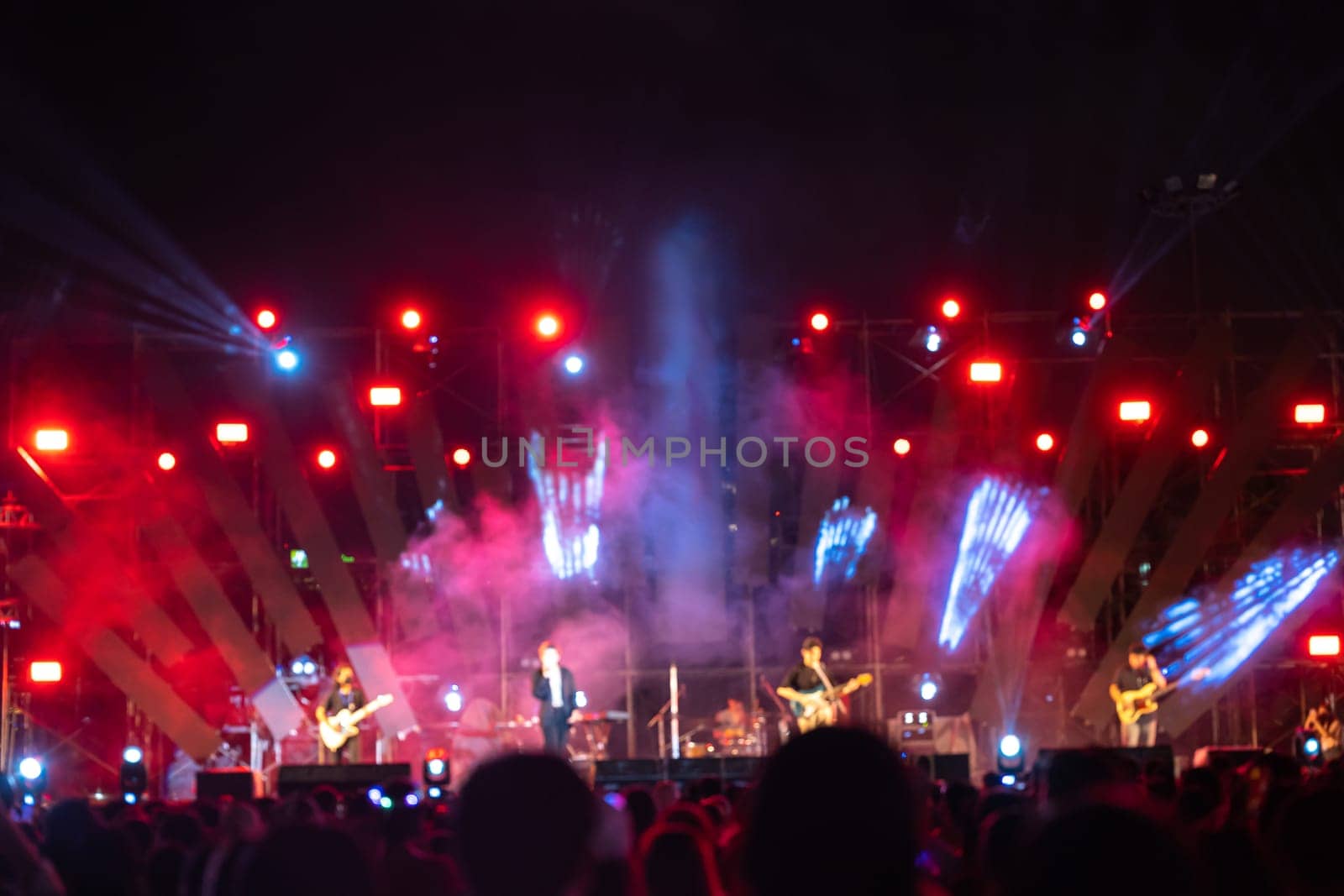 In heart of night concert festival main event lights up with cheering unrecognizable crowd in front of brilliantly illuminated stage. lens flare enhances excitement of this lively music event.