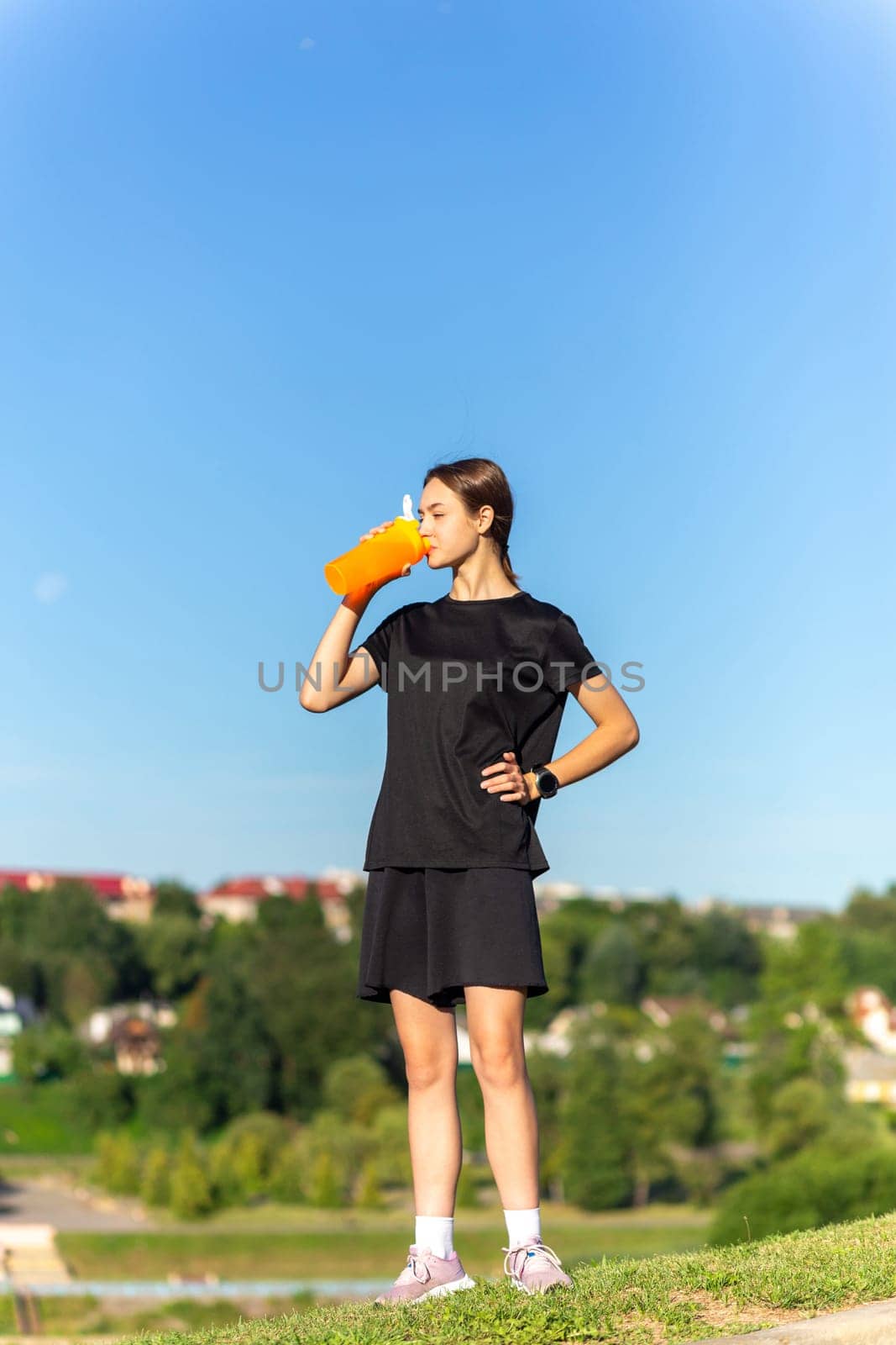 Fit tennage girl runner outdoors holding water bottle. Fitness woman taking a break after running workout.