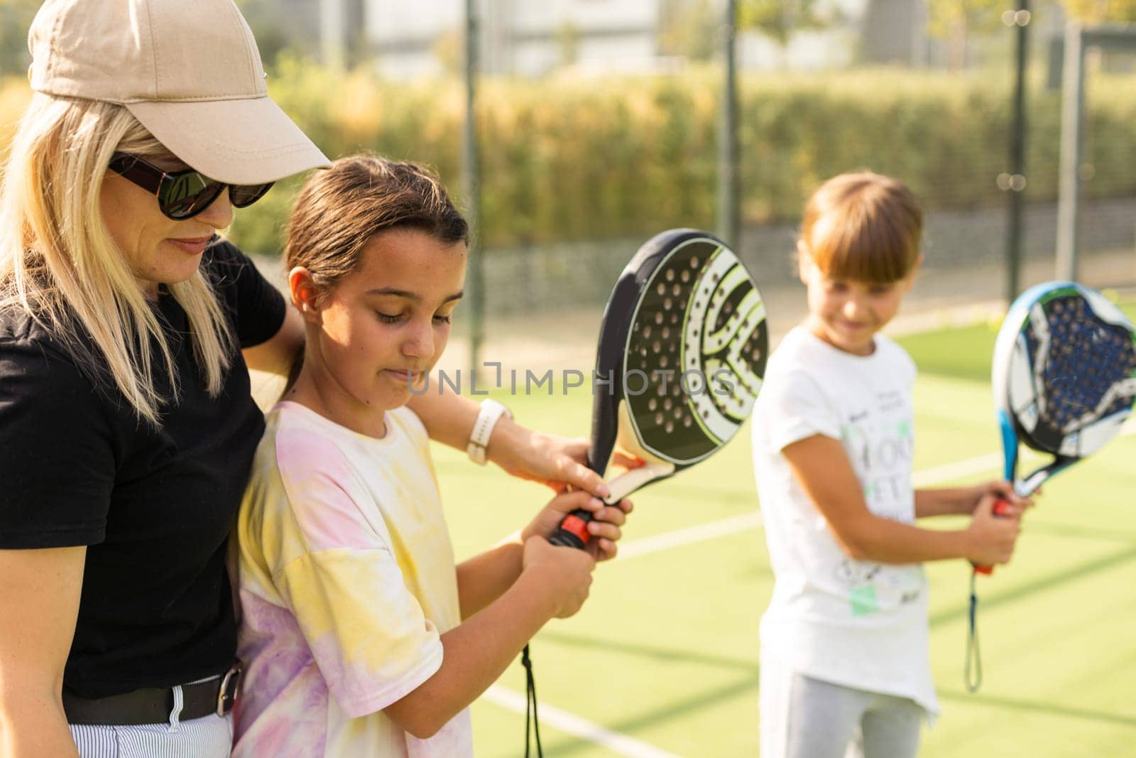 Young sporty woman with children playing padel game in court on sunny day by Andelov13
