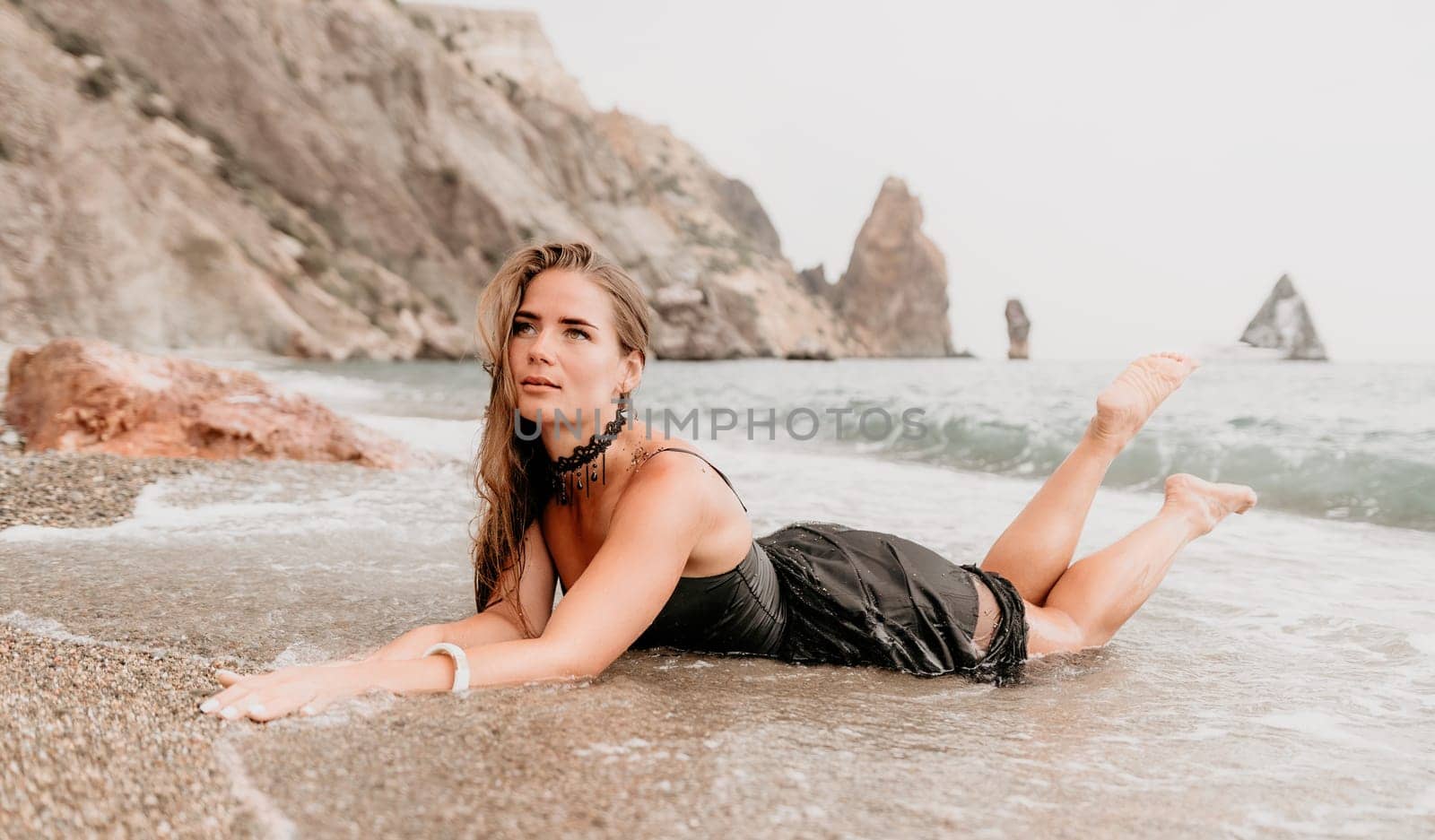 Woman travel sea. Young Happy woman in a long red dress posing on a beach near the sea on background of volcanic rocks, like in Iceland, sharing travel adventure journey